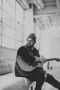 picture of dave hinrich sitting on couch holding guitar