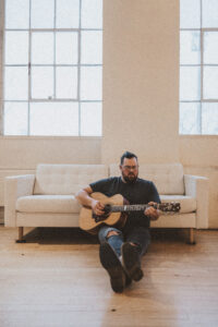 picture of dave hinrich with guitar in front of couch